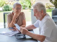 Seniorzy przynieśli listy, by otworzyć je przy stole. Mężczyzna czyta treść jednego z nich, kobieta jest wyraźnie przejęta. | Fot. Shutterstock.