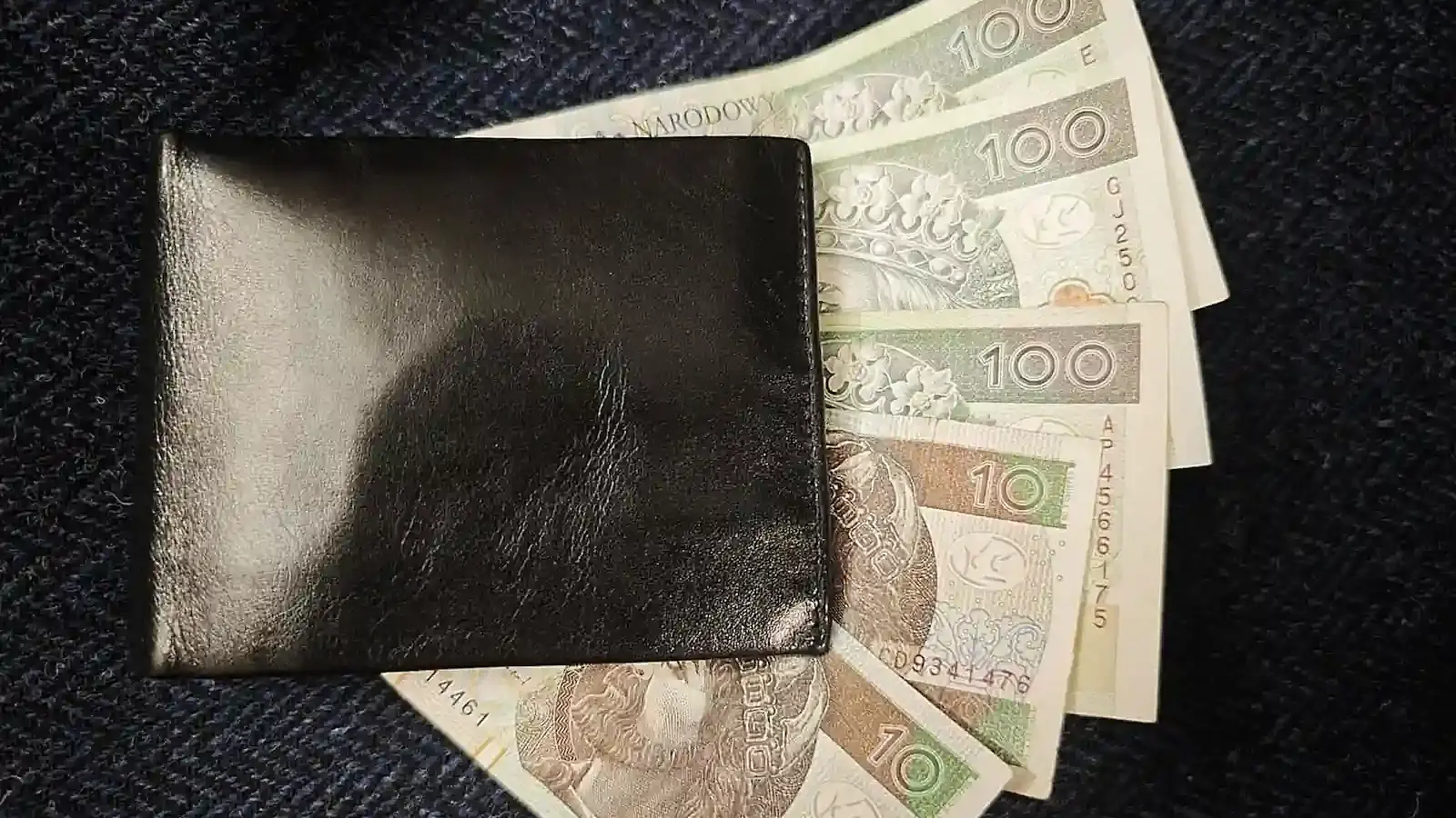Gotówka włożona w portfel leży na granatowej marynarce. Fot. Warszawa w Pigułce.