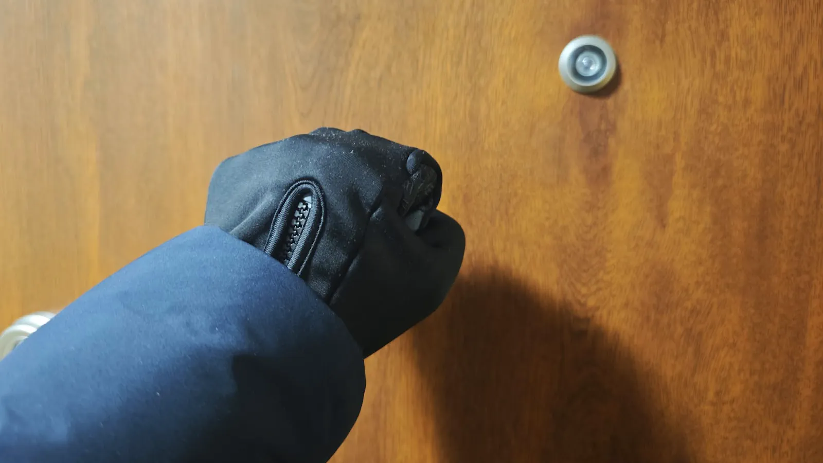 Mężczyzna w rękawiczkach i kurtce pukający do drzwi mieszkania. Fot. Warszawa w Pigułce