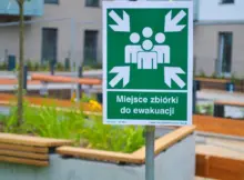 Warszawa, Polska - 16 września 2025 r.: Zdjęcie zielonego znaku punktu zbiórki ewakuacyjnej z ikonami ludzi i strzałkami skierowanymi do wewnątrz.