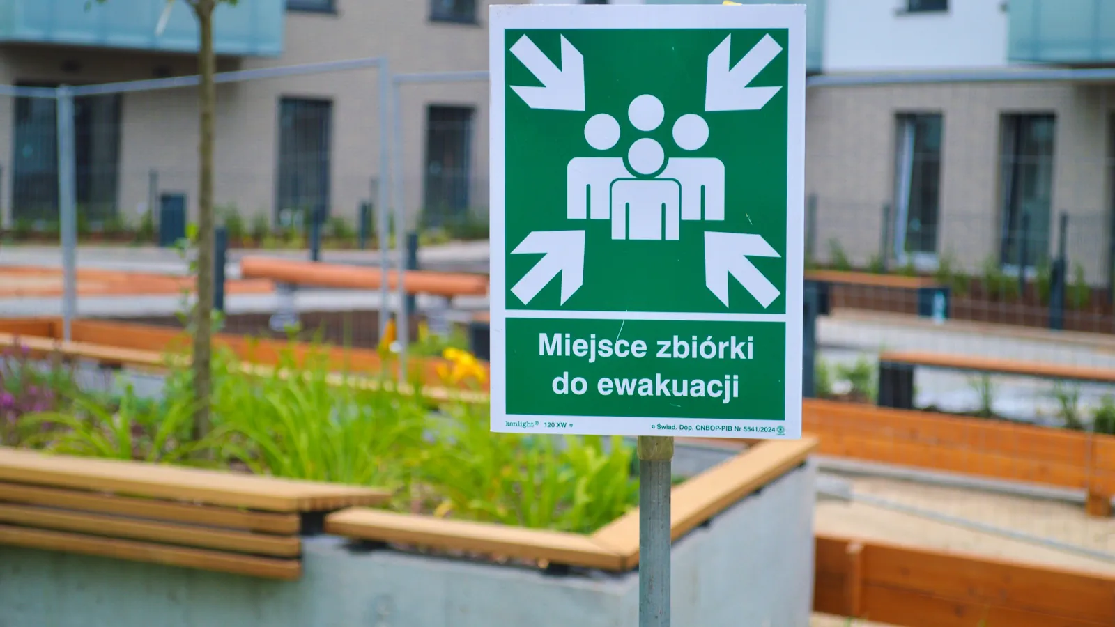 Warszawa, Polska - 16 września 2025 r.: Zdjęcie zielonego znaku punktu zbiórki ewakuacyjnej z ikonami ludzi i strzałkami skierowanymi do wewnątrz.